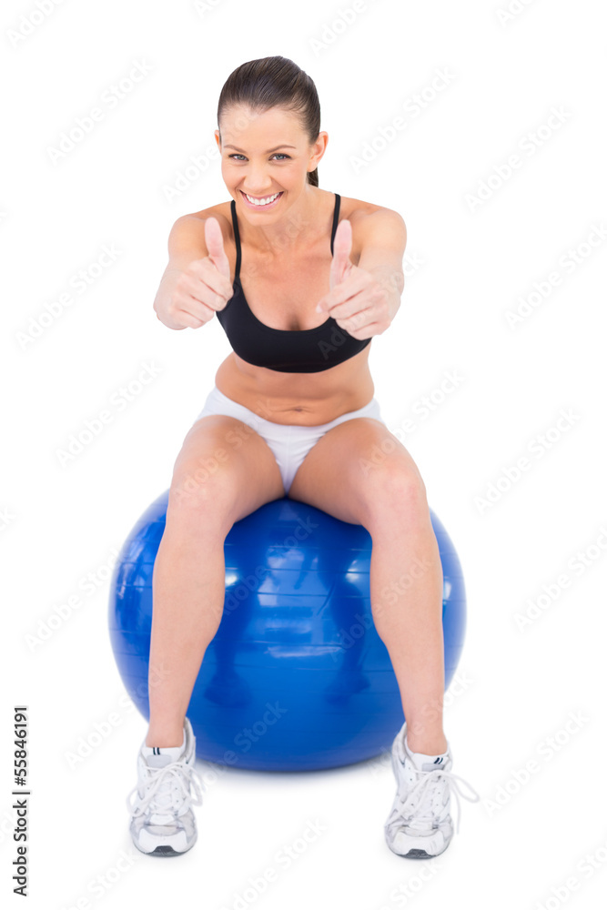 Positive woman in sportswear sitting on exercise ball giving thu Positive woman in sportswear sitting on exercise ball giving thu