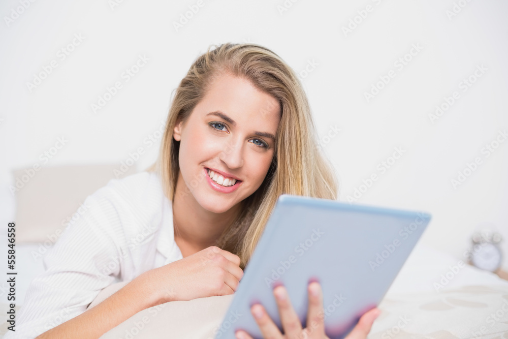 Smiling pretty model using her tablet pc lying on cosy bed Smiling pretty model using her tablet pc lying on cosy bed