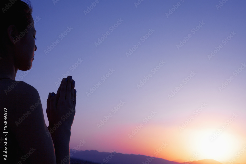 Serene young woman with hands together in prayer pose  in the desert in China, silhouette, sun setting