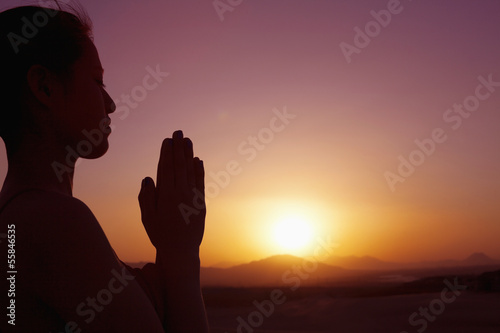Serene young woman with hands together in prayer pose  in the desert in China, silhouette, sun setting, profile