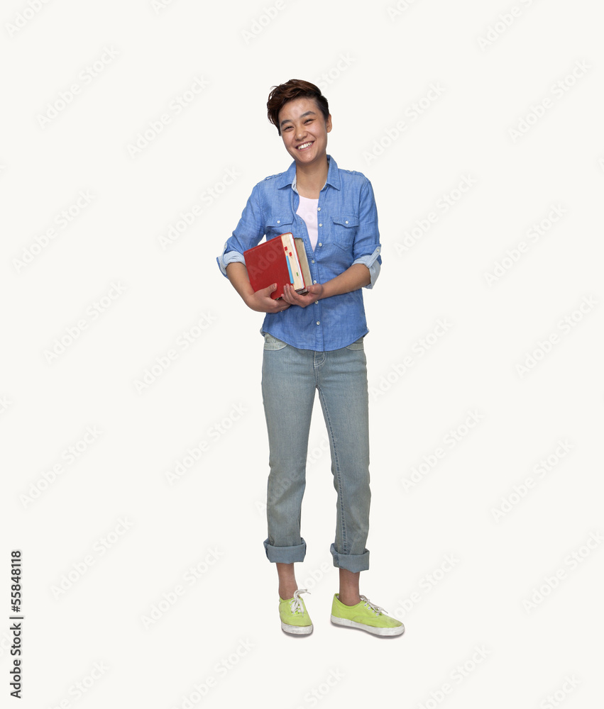Portrait of smiling young female student holding books, studio shot, full length