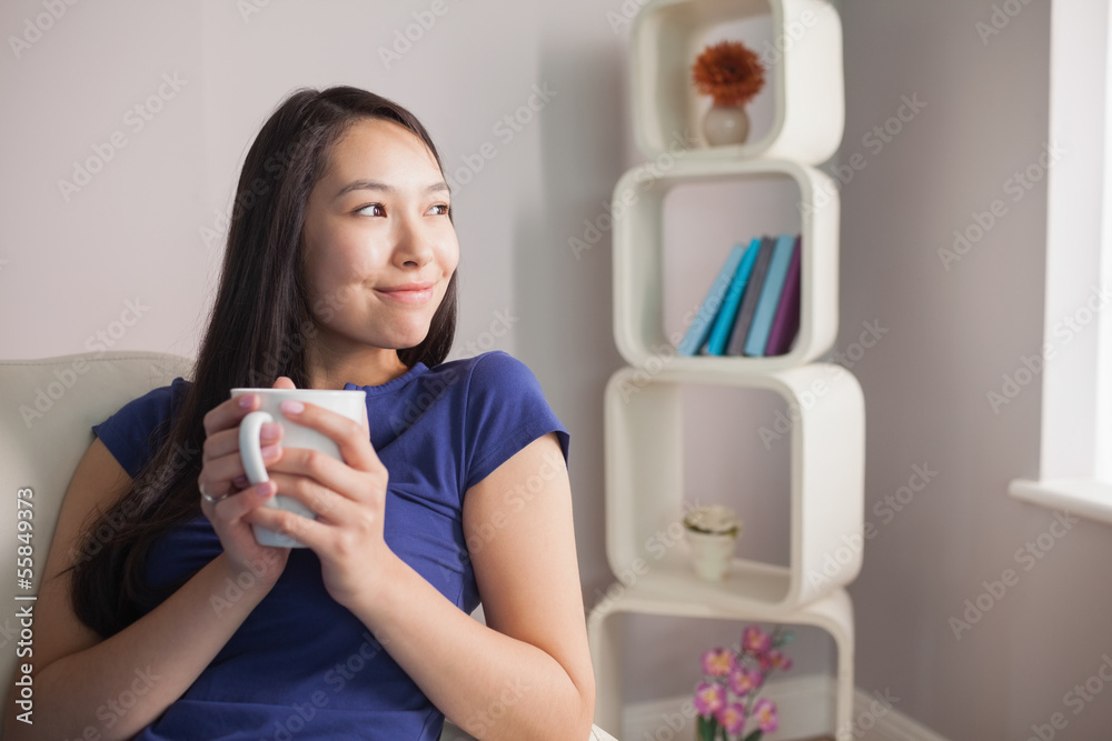 Thinking young asian woman sitting on the couch holding mug Thinking young asian woman sitting on the couch holding mug