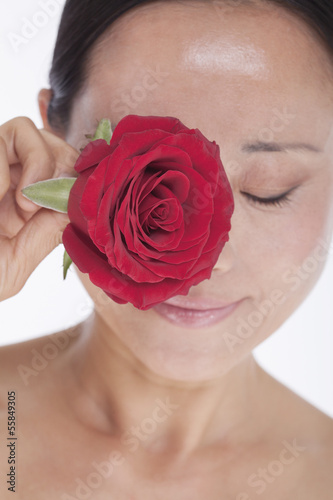 Smiling  beautiful  shirtless woman holding a red rose to her eye  studio shot