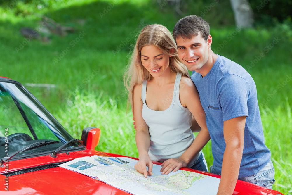 Cheerful young couple reading map on their cabriolet bonnet Cheerful young couple reading map on their cabriolet bonnet
