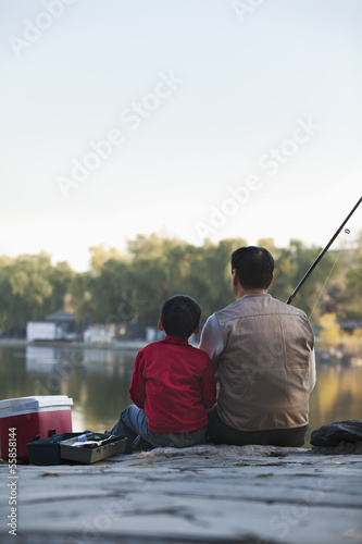 Grandfather and grandson sitting and fishing at a lake