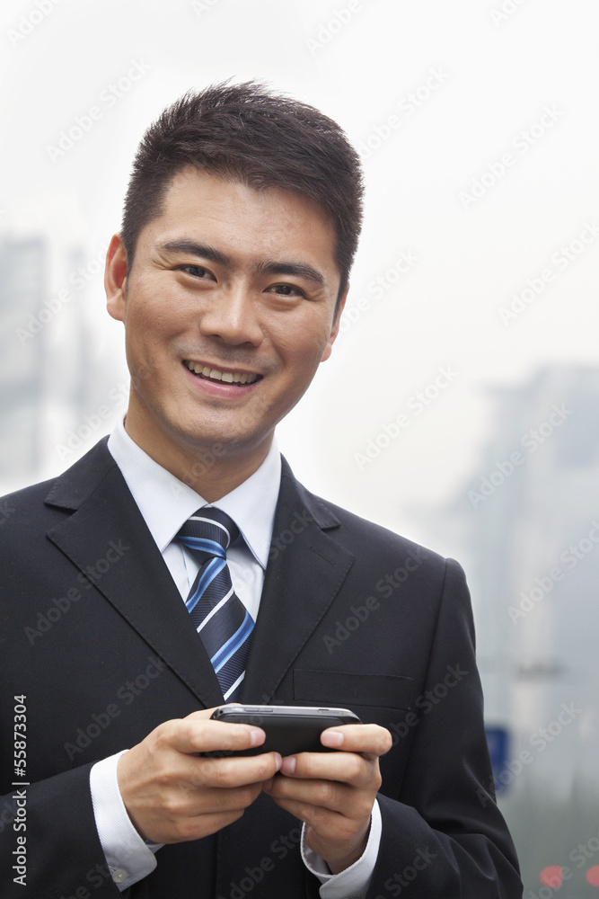 Young Businessman Smiling and Using a Smart Phone, Looking at Camera Young Businessman Smiling and Using a Smart Phone, Looking at Camera