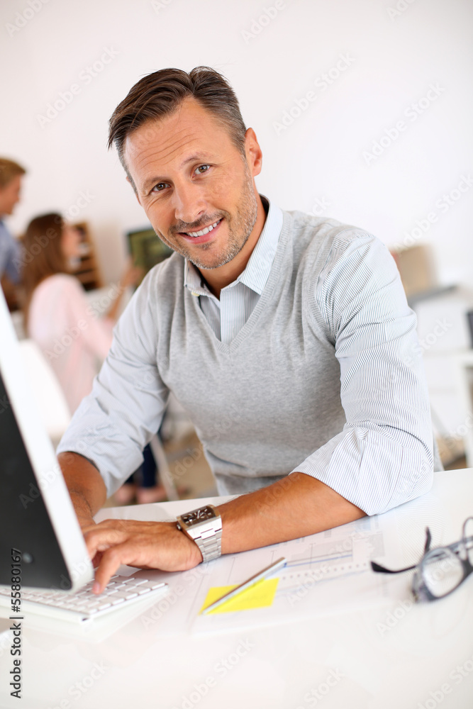 Cheerful man sitting in office and working on desktop Cheerful man sitting in office and working on desktop