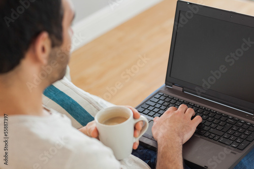 Brown haired man holding coffee using his laptop