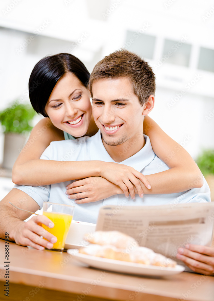 Woman embraces eating boyfriend who sits at the kitchen