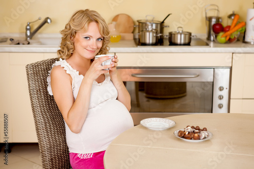 Young pregnant woman drinks tea with sweets at kitchen