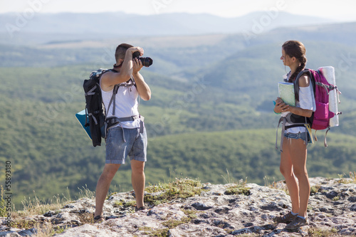 Two tourists. Man photographs woman, she is holding a map.