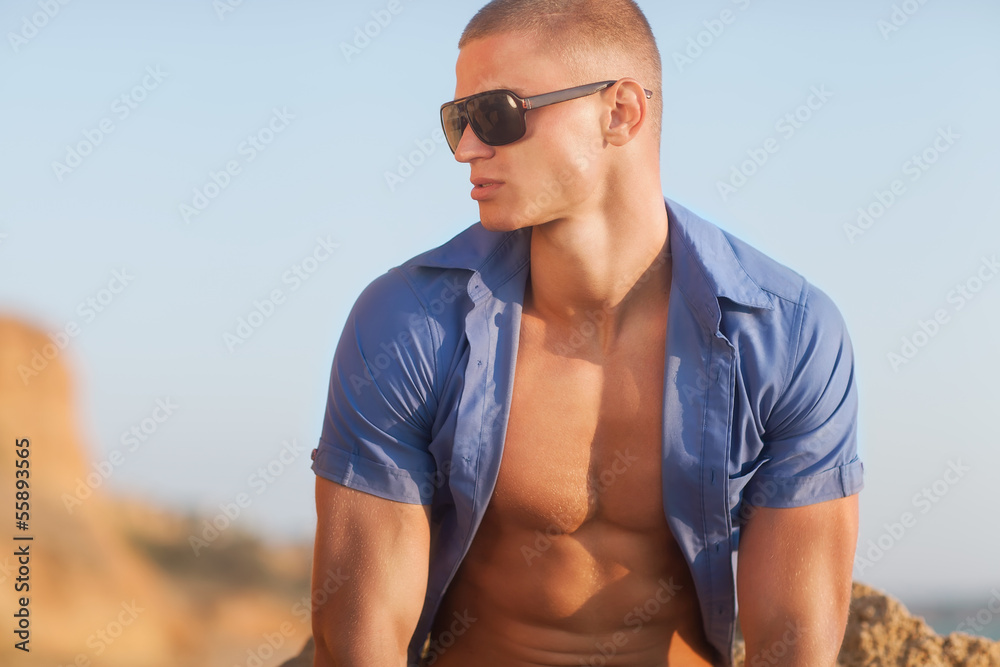Young muscular man sitting on the beach. Young muscular man sitting on the beach.