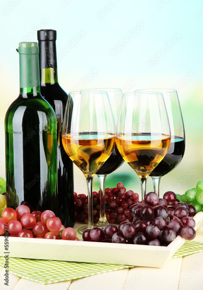 Wine bottles and glasses of wine on tray, on bright background