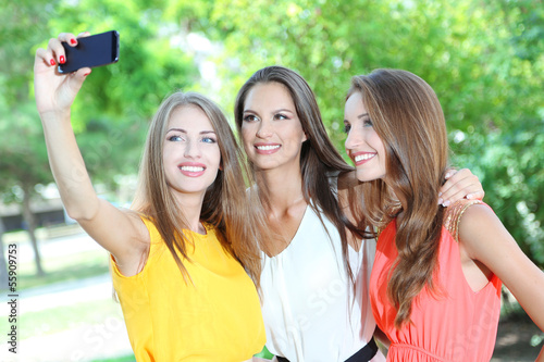 Three beautiful young woman taking picture in summer park
