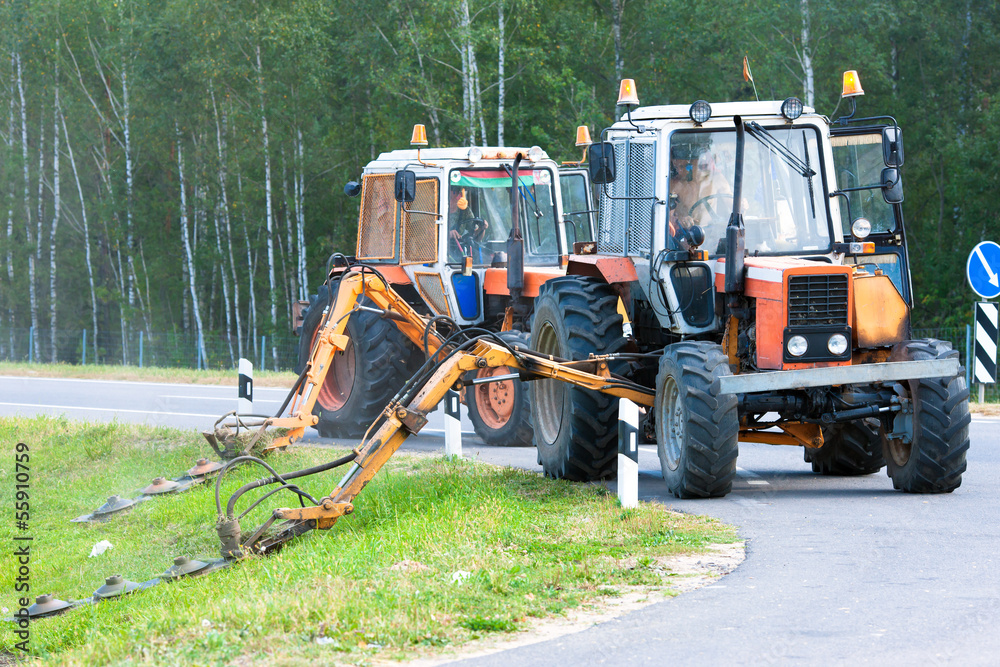 Obraz premium Tractors machines mowing lawn grass along road