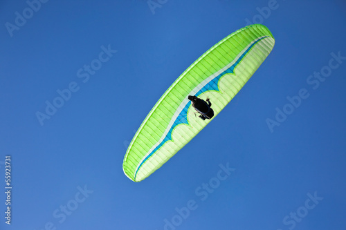 Green paraglider flying in blue sky.