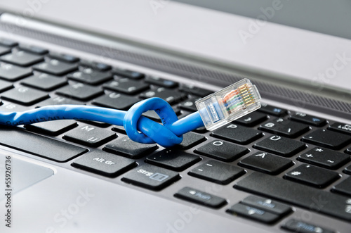 Netzwerkkabel mit Knoten auf Computer Tastatur als Symbol für langsames oder gestörtes Internet/Netzwerkverbindung
