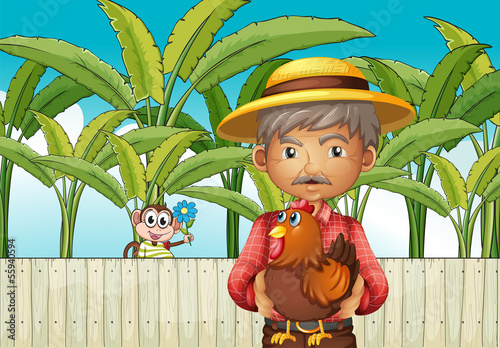 An old man holding a rooster standing in front of the fence with