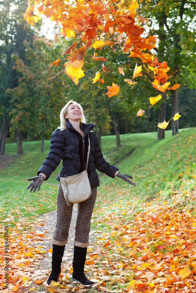 The beautiful woman in autumn park throws up red maple leaves.. The beautiful woman in autumn park throws up red maple leaves..