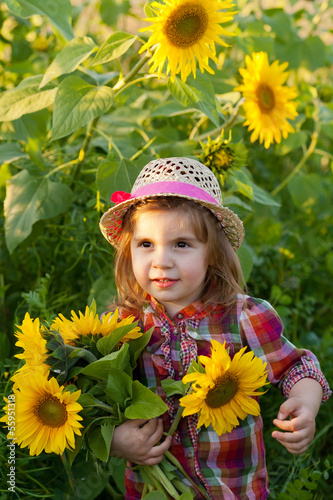 Little girl in a summer hat among sunflowers