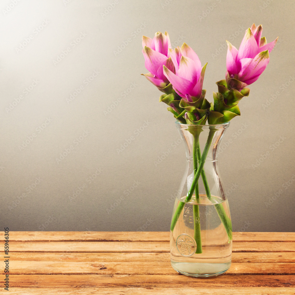 Obraz premium Pink tropical flowers in glass vase on wooden table