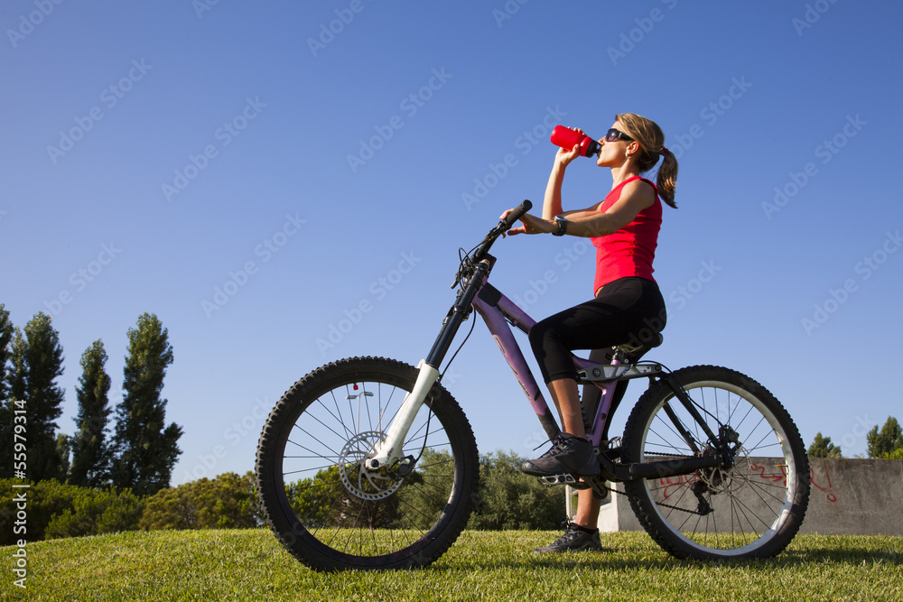 young woman in a bicycle drinking water at the park