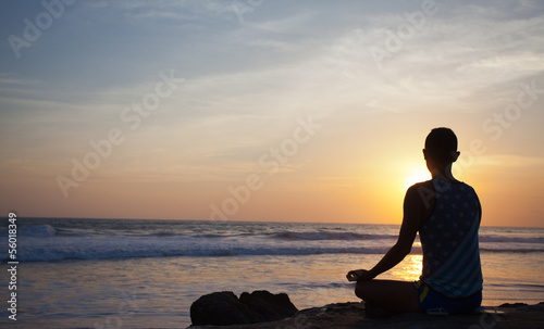 sitting man doing yoga on shore of ocean