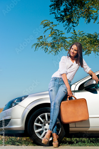 Beautiful woman with suitcase leaning on a car