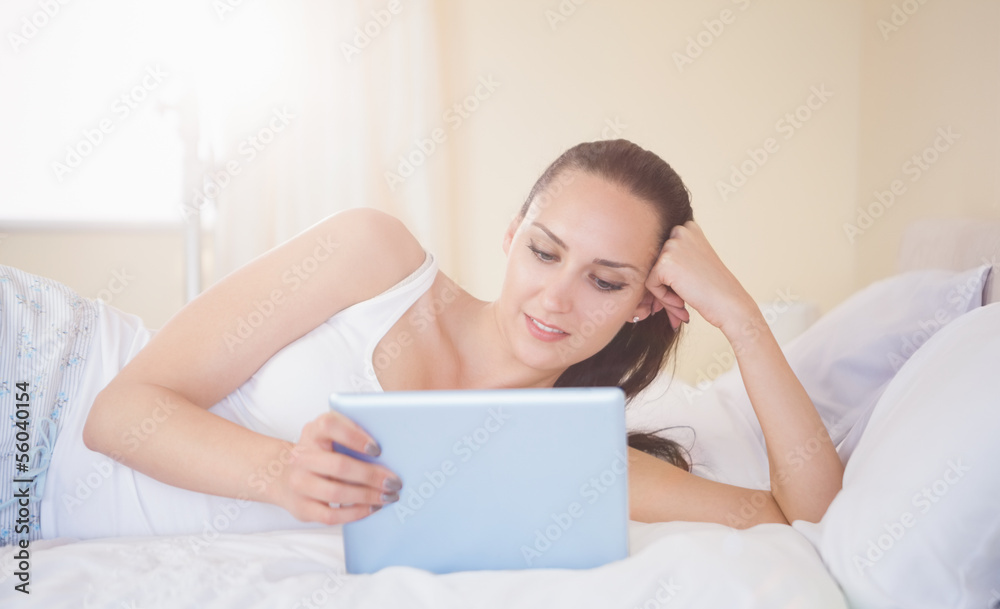 Content brunette lying on bed using her tablet pc Content brunette lying on bed using her tablet pc