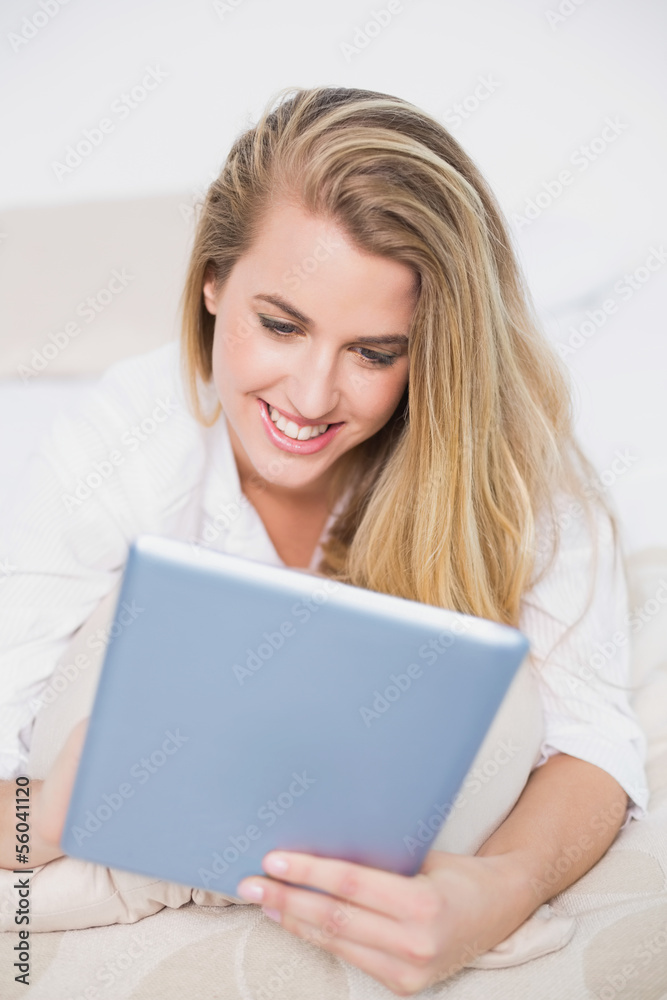 Cheerful model using her tablet lying on cosy bed Cheerful model using her tablet lying on cosy bed