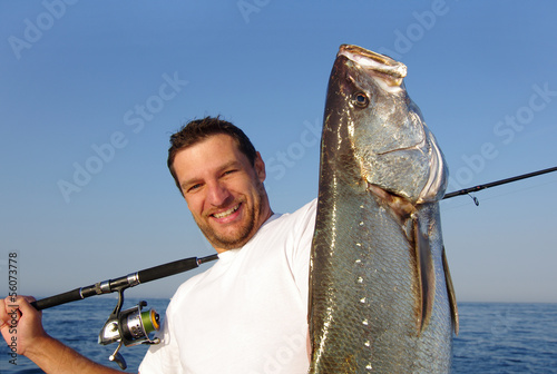 Pêcheur en mer tenant un  gros maigre (courbine)