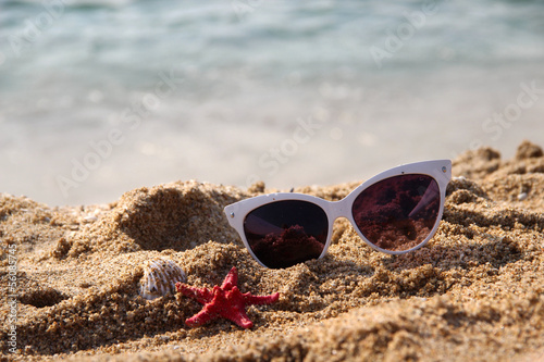 Mix of vivid starfishes on the beach and female sunglasses