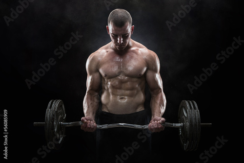 Young muscular man lifting weights over dark background