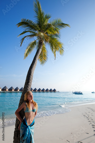 Young beautiful woman stands near palm tree, Maldives