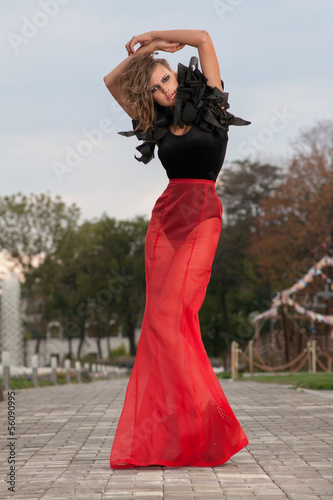 Fashionable model posing in long red and black dress outdoors