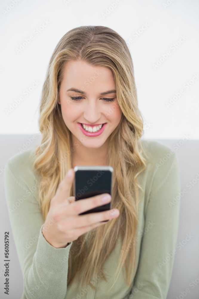 Smiling pretty blonde sending a text sitting on cosy sofa Smiling pretty blonde sending a text sitting on cosy sofa