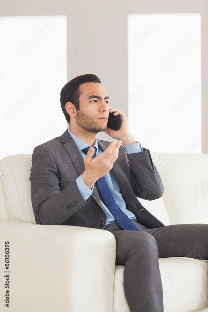 Serious businessman having a phone call sitting on cosy sofa