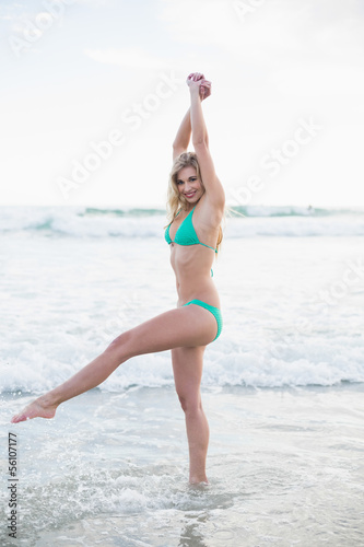 Joyful blonde woman in green bikini playing in the waves