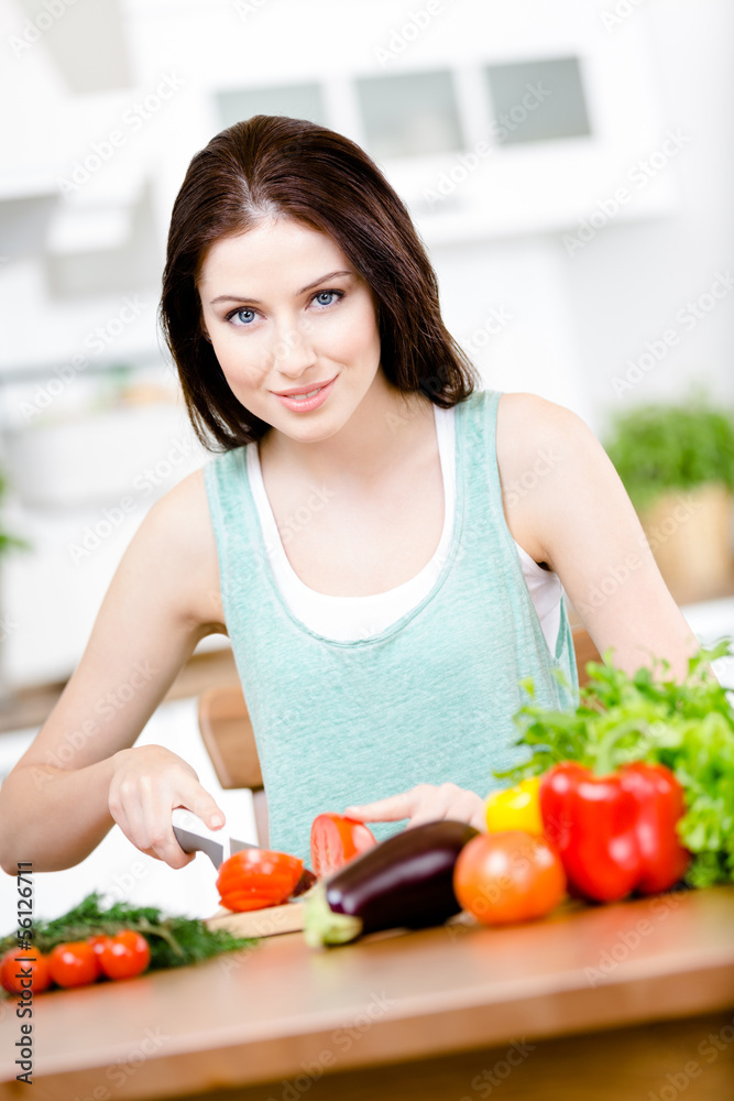 Girl cuts vegetables for salad sitting at the kitchen table