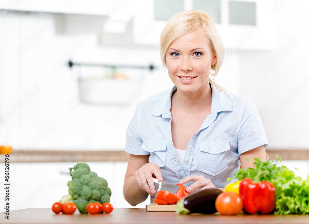Woman cuts vegetables for salad sitting at the kitchen