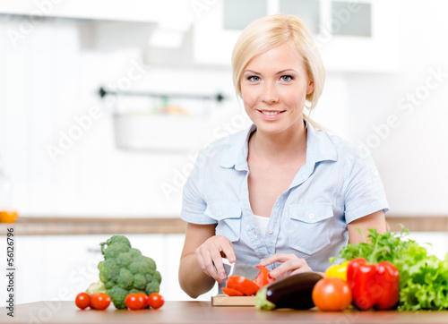 Woman cuts vegetables for salad sitting at the kitchen