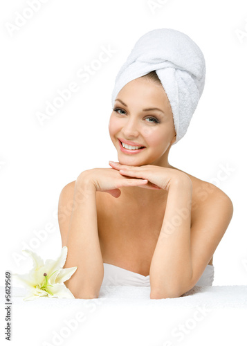 Girl with towel on head touches face sitting near a white lily