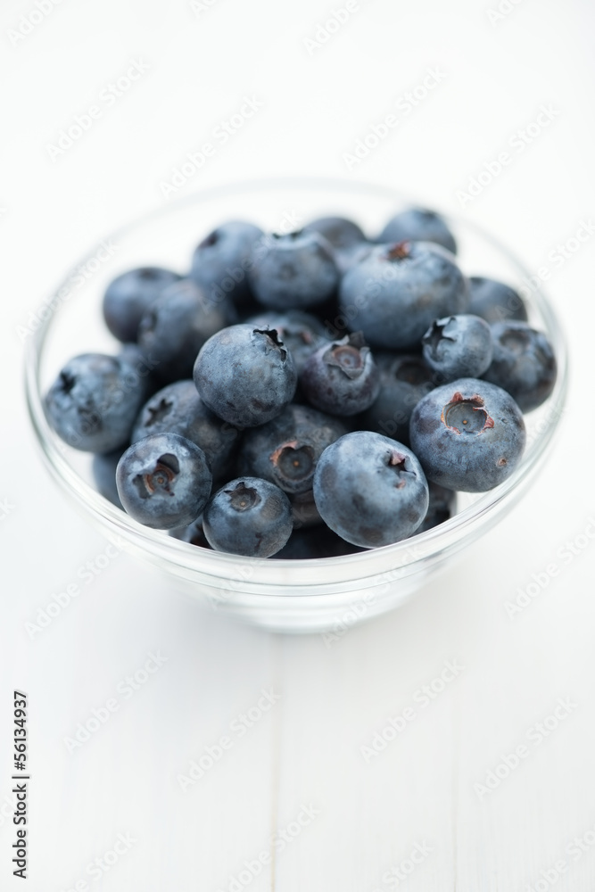 Glass bowl full of ripe blueberries on white wooden background Glass bowl full of ripe blueberries on white wooden background