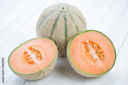 Whole and halved cantaloupe melons on white wooden background