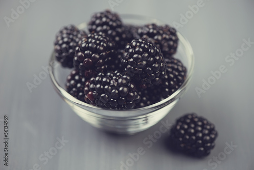 Glass bowl with ripe blackberries on grey wooden background