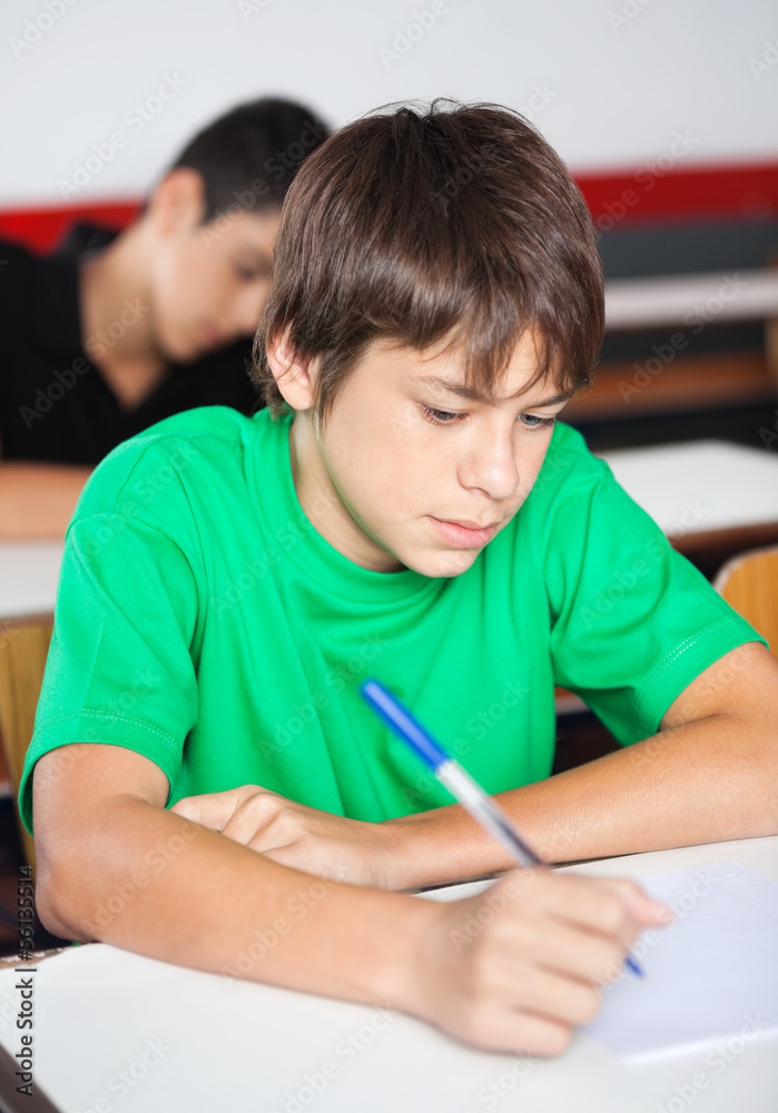 Teenage Schoolboy Writing At Desk During Examination Teenage Schoolboy Writing At Desk During Examination