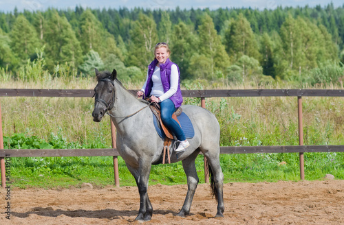 Beautiful smiling girl riding a gray horse