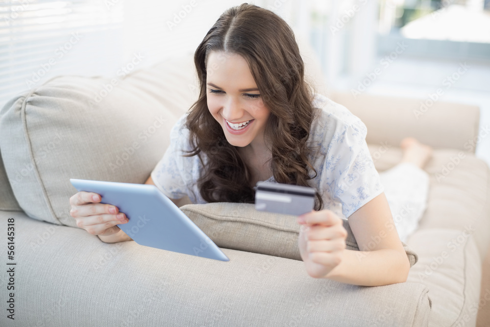 Smiling woman lying on a cosy couch buying online Smiling woman lying on a cosy couch buying online
