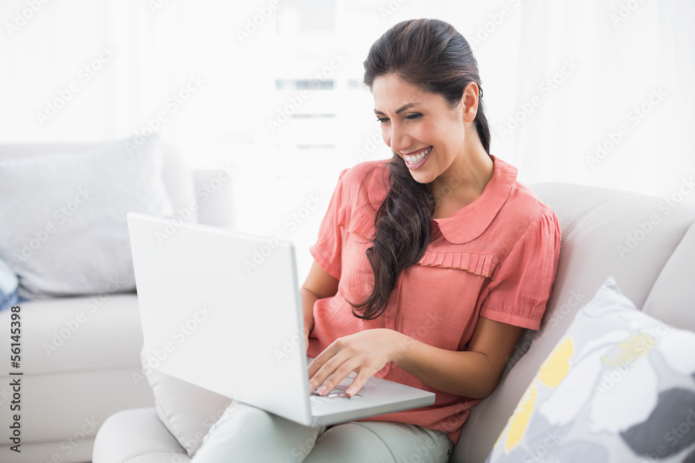 Happy brunette sitting on her sofa using laptop Happy brunette sitting on her sofa using laptop