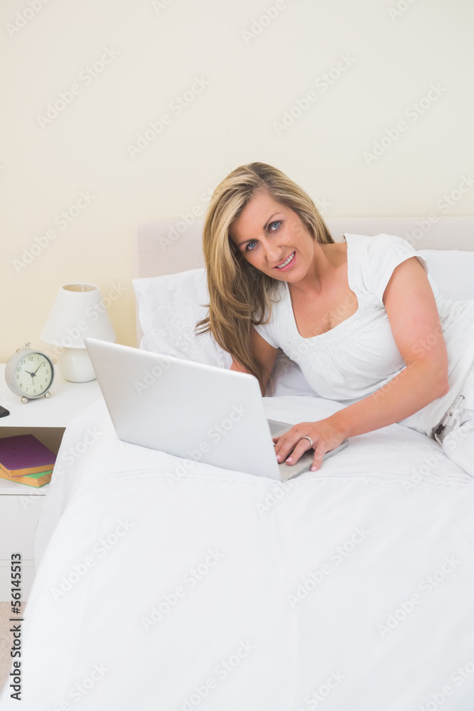 Content woman using a laptop lying on her bed